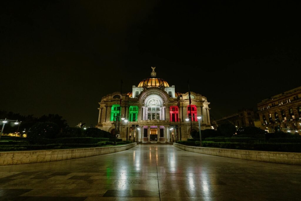 Palacio de Bellas Artes illuminated in Mexican flag colors at night.